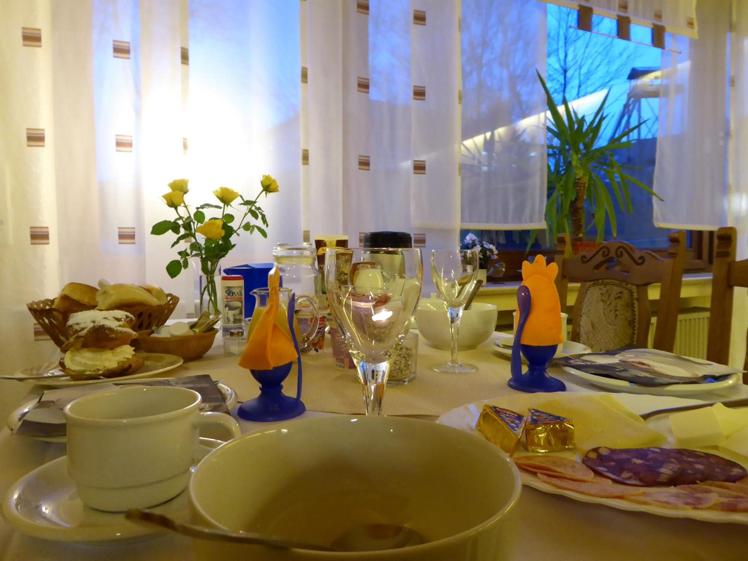 Ein Esstisch ist reichhaltig mit Geschirr, Gläsern und einer Blumenvase gedeckt.