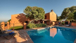 A swimming pool with lounge chairs, a clear sky, and a building with a tiled roof. - La Casa del Torero (Vejer de la Frontera)