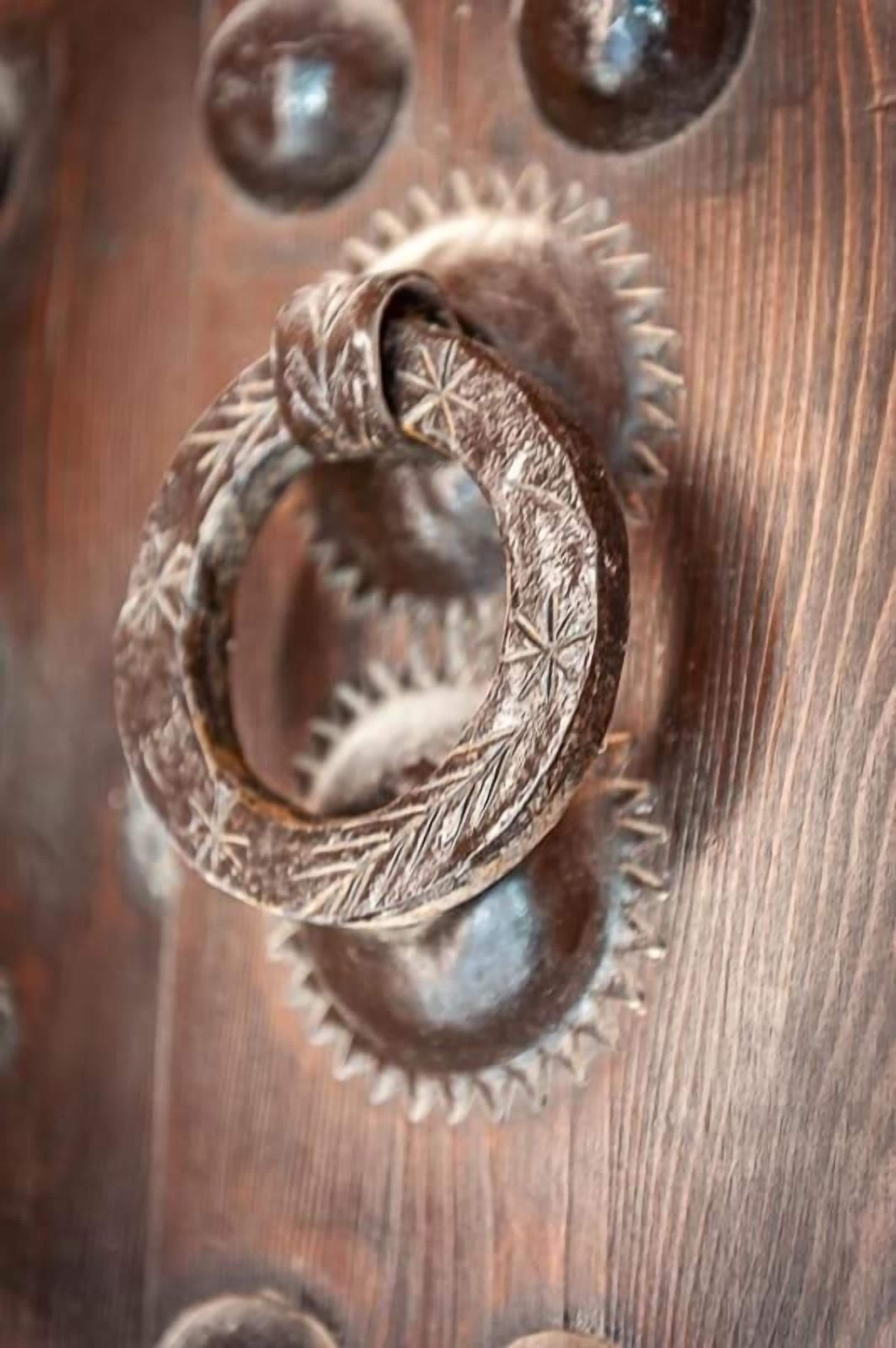 Primer plano de una puerta de madera con un pomo metálico circular decorado con diseños intrincados.