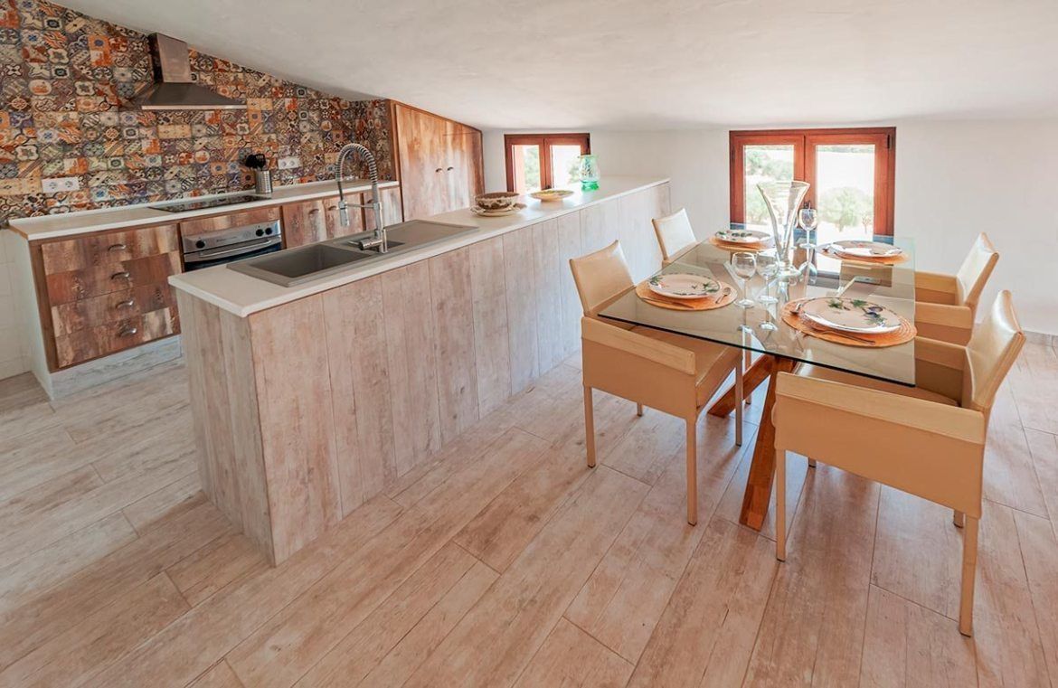 A modern kitchen with a central island, wooden cabinets, and a dining area with a glass table and chairs.