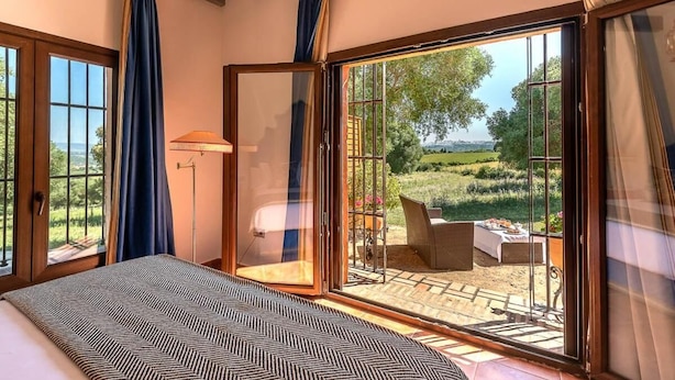 A bedroom with a large bed, a view of the garden through a glass door, and a patio area with outdoor furniture. - La Casa del Torero (Vejer de la Frontera)