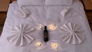 A neatly made bed with white linens, a bottle of alcohol, and multiple lit candles arranged in a circular pattern. - Airport View Apartments (Belgrade)
