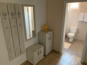 A bathroom with a toilet, a sink, and a mirror. There is a cabinet with a yellow lamp on top. The floor is tiled, and the walls are painted beige.