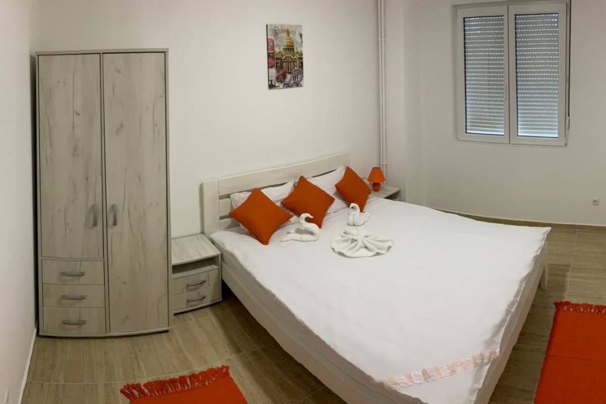 A bedroom with a bed, a wardrobe, a nightstand, and a window with blinds.