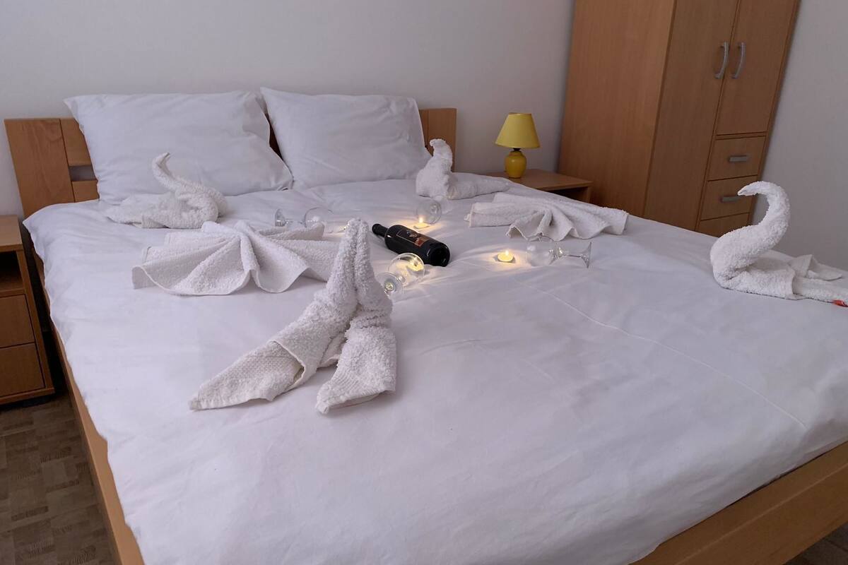A neatly made bed with white towels arranged in swan shapes, a bottle of water, and a wine glass on the bed.