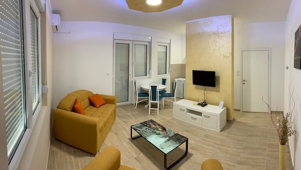 A modern living room with a sofa, coffee table, TV, and a small dining area. - Airport View Apartments (Belgrade)
