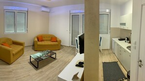 A living room with two yellow sofas, a coffee table, and a TV. There is a kitchen area with cabinets and a countertop. - Airport View Apartments (Belgrade)