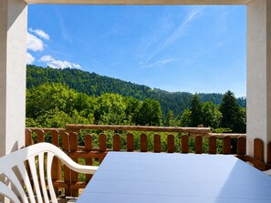 Un balcone con tavolo e sedie, affacciato su una montagna boscosa.