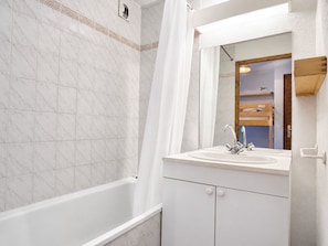 A bathroom with a bathtub, a sink with a mirror, and a shower curtain.