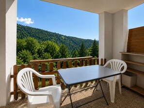 Un balcón con mesa y sillas, con vistas a una ladera boscosa.