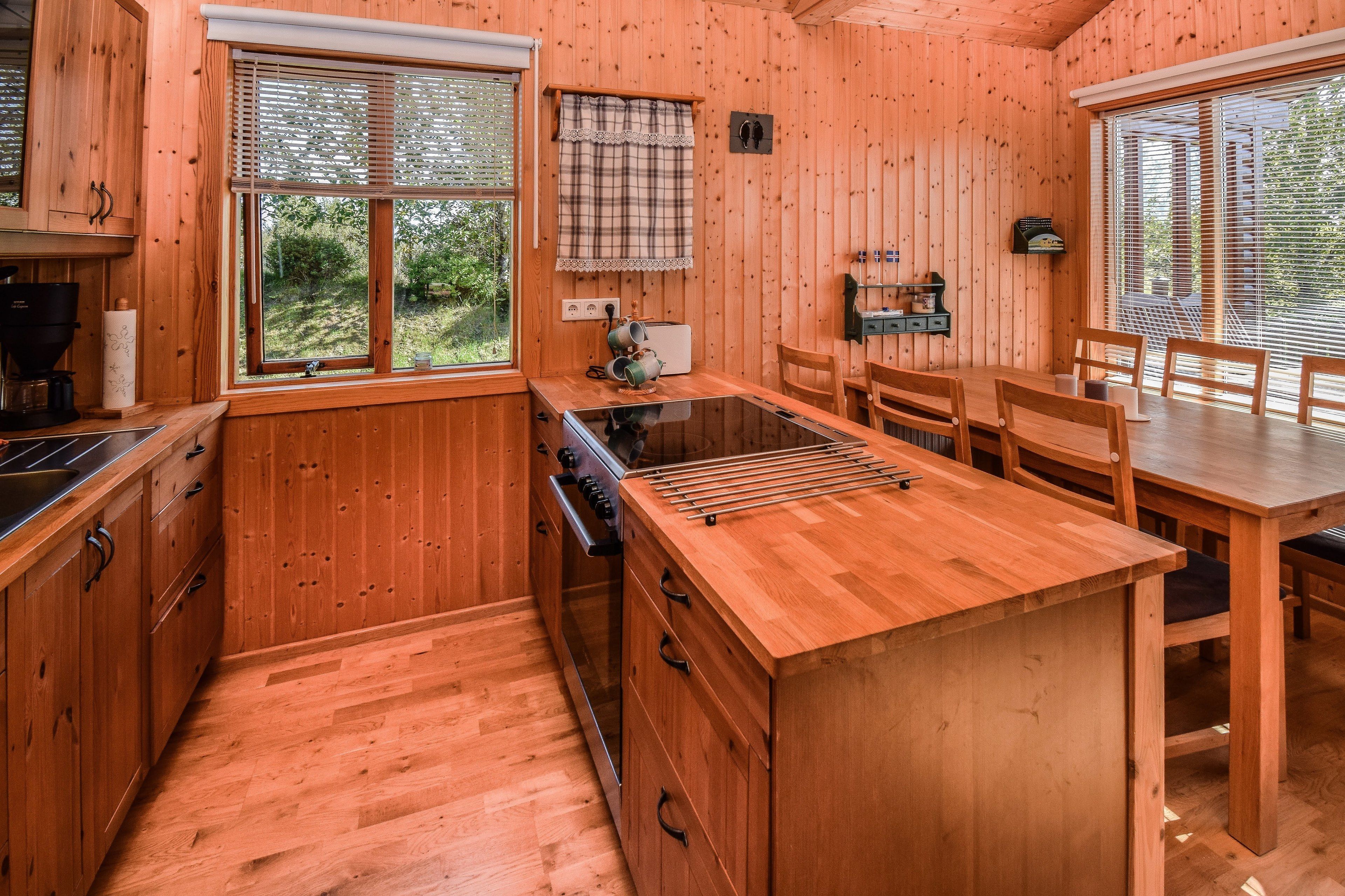 A wooden cabin kitchen with a central island, wooden cabinets, a stove, and a dining area with chairs and a table.