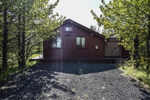 A cabin with a gravel driveway, surrounded by trees. - Cottage O12 (Selfoss)