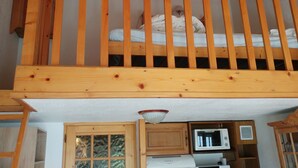 Une chambre de style loft avec une rambarde en bois, un lit superposé et un coin cuisine équipé d’un micro-ondes et de placards.