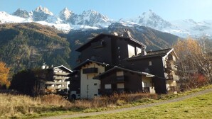 Un immeuble à étages, de style architectural traditionnel, situé dans une région montagneuse, avec des sommets enneigés en arrière-plan.