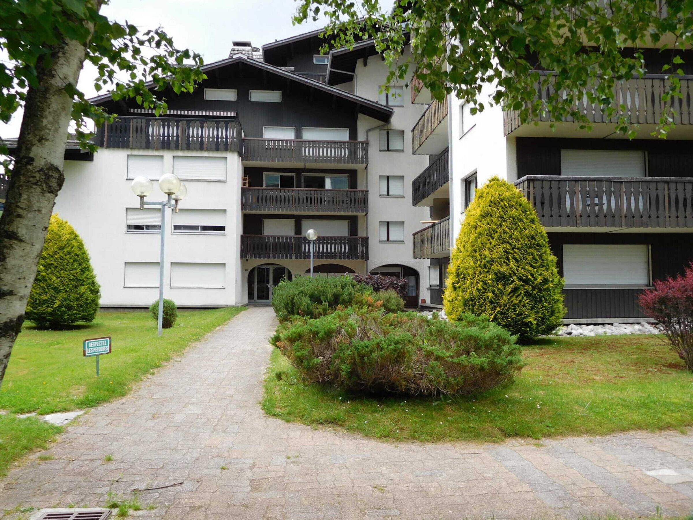 A multi-story residential building with balconies, a paved entrance, and well-maintained greenery.