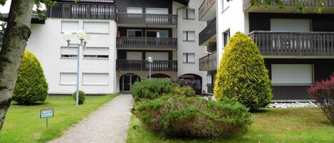 A multi-story residential building with balconies, a paved entrance, and well-maintained greenery.