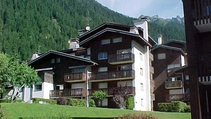 Un edificio de varios pisos con balcones, rodeado de vegetación y montañas.
