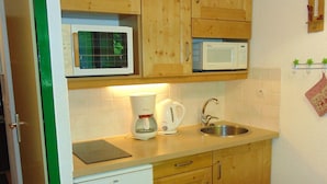 A compact kitchen with wooden cabinets, a microwave, a coffee maker, and a sink. - Studio Chamonix 20m², 4 pers, balcony, parking (Chamonix-Mont-Blanc)