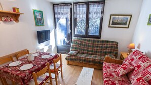 A cozy living room with a dining table set for four, a sofa, and a television. - Studio Chamonix 20m², 4 pers, balcony, parking (Chamonix-Mont-Blanc)