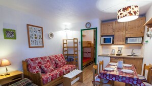 A compact room with a sofa, a dining table set for two, a bunk bed, and a kitchenette. - Studio Chamonix 20m², 4 pers, balcony, parking (Chamonix-Mont-Blanc)