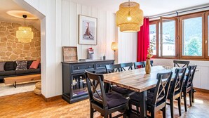A dining area with a wooden table and chairs, a stone wall, and a red curtain. - Stunning downtown apartment - Pets allowed, WiFi (Chamonix-Mont-Blanc)