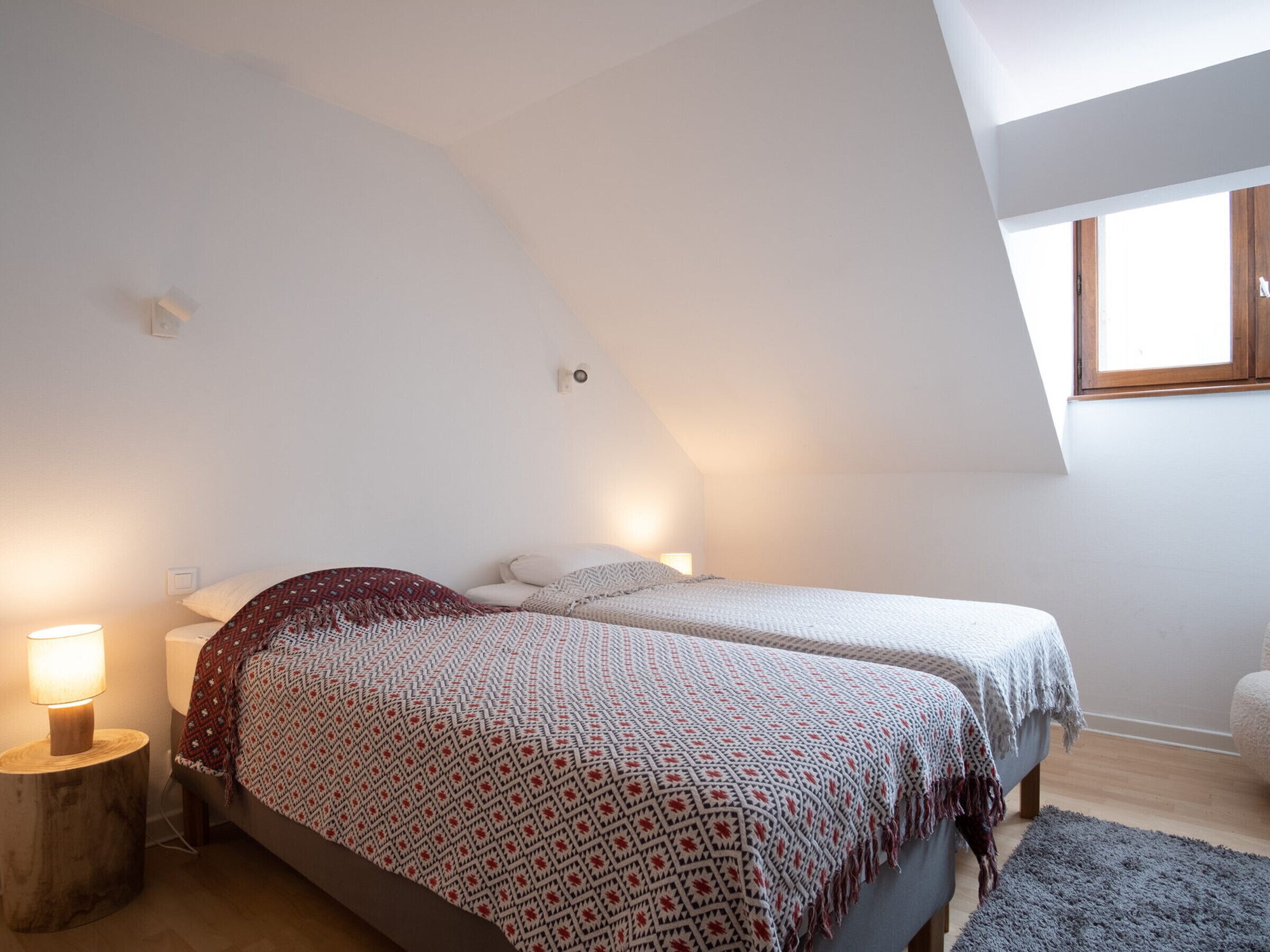 A bedroom with two beds, a window, and a lamp.