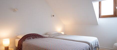 A bedroom with two beds, a window, and a lamp.