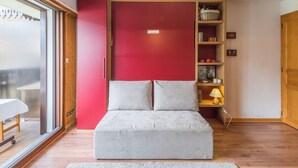 A room with a grey sofa, a red cabinet, and a wooden floor.