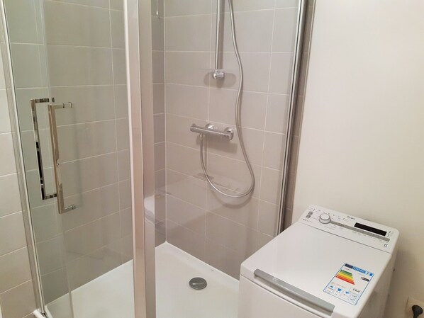 A bathroom with a glass-enclosed shower, a white tiled wall, and a white washing machine.