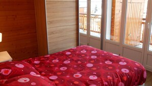 Ein Zimmer mit einem Bett, das mit einer rot gepunkteten Bettdecke bezogen ist, Holzwänden und einem Fenster mit Blick auf eine Holzterrasse.