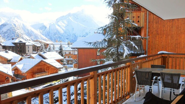 Ein Holzbalkon mit Blick auf schneebedeckte Berge und Gebäude.
