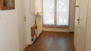 Ein Flur mit Holzboden, einer weißen Tür, einem Spiegel, einem Regal mit einem kleinen Gegenstand und einem Fenster mit Blick auf ein Gebäude.