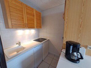Une cuisine de taille réduite, dotée de meubles en bois, d’un plan de travail blanc, d’un lave-vaisselle et d’une machine à café.