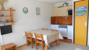 A compact kitchen with white cabinets, a microwave, and a stove. There is a dining table with chairs and a small wooden stool.
