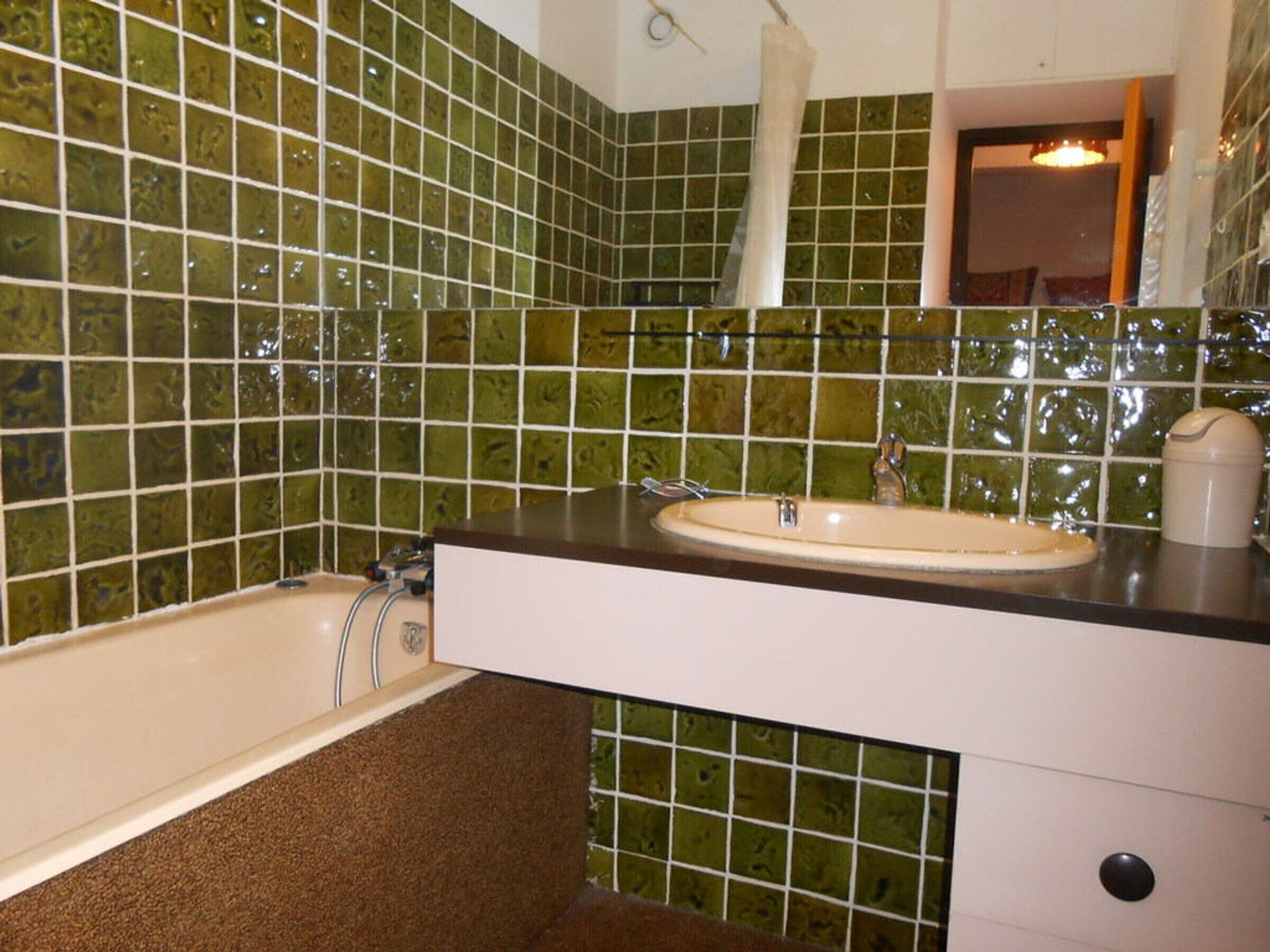 A bathroom with green mosaic tiles, a white sink, and a bathtub.