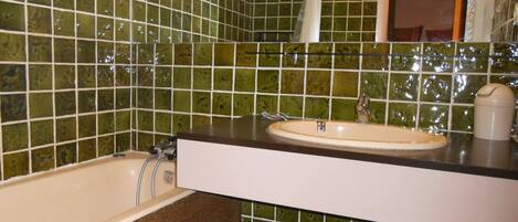Ein Badezimmer mit grünen Mosaikfliesen, einem weißen Waschbecken und einer Badewanne.
