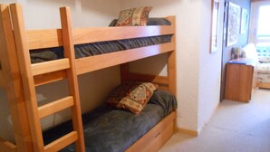A bunk bed with a ladder, a single bed below, and a small wooden nightstand.