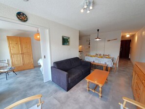 A living room with a sofa, dining table, and chairs, a wooden wardrobe, and a hanging light fixture.