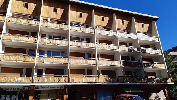 Un hotel de varios pisos con balcones, una tienda a nivel de calle y coches estacionados.