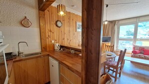 A kitchen with wooden cabinets, a sink, and a kettle. There is a dining area with chairs and a table. - Studio for 4, center of Les Deux Alpes, pets allowed (Les Deux Alpes)