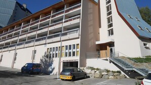 A multi-story building with a flat roof, a staircase leading to the upper floors, and a parking area with cars. - Studio for 4, center of Les Deux Alpes, pets allowed (Les Deux Alpes)