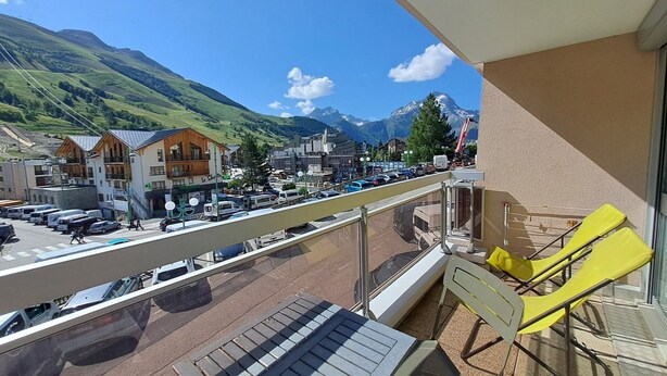 A balcony with a view of a mountain, a road with vehicles, and buildings. - Studio for 4, center of Les Deux Alpes, pets allowed (Les Deux Alpes)