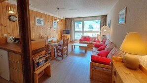 A cozy room with wooden walls, a dining area, a sofa with red cushions, a lamp, and a television. - Studio for 4, center of Les Deux Alpes, pets allowed (Les Deux Alpes)