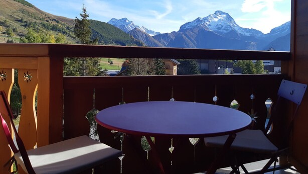 Un balcon avec une table ronde et des chaises, donnant sur un paysage montagneux aux sommets enneigés.