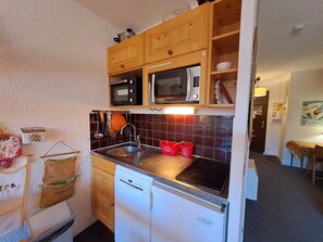 A compact kitchen with wooden cabinets, a microwave, a dishwasher, and a tiled backsplash.
