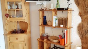 Un meuble en bois doté de portes en verre, contenant de l’ustensile de cuisine, un téléviseur fixé au mur et une étagère avec des livres et des objets décoratifs.
