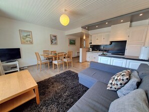 A modern living room with a sofa, television, dining table, and chairs.