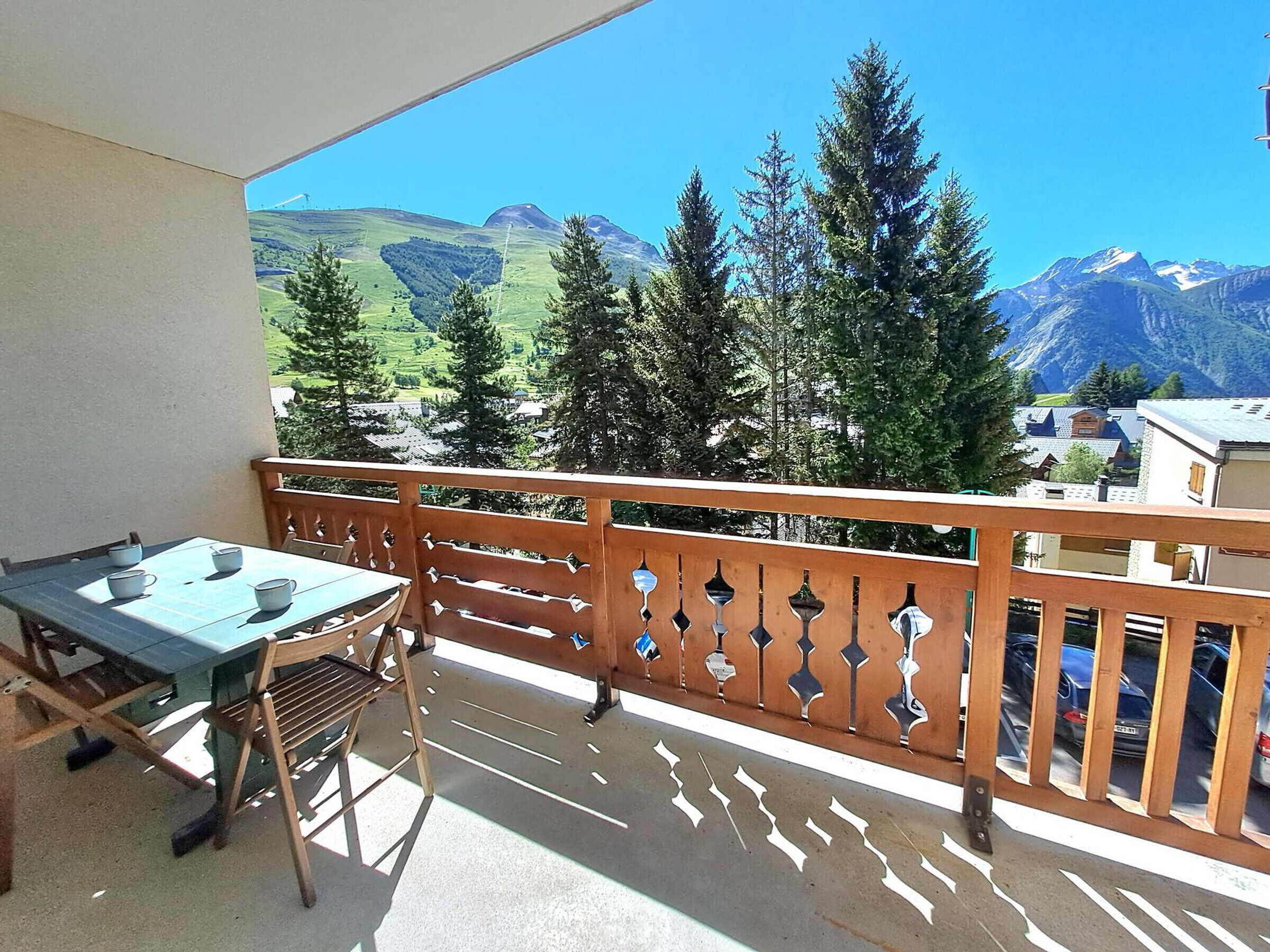 A balcony with a table and chairs, overlooking a mountainous landscape with trees and buildings.