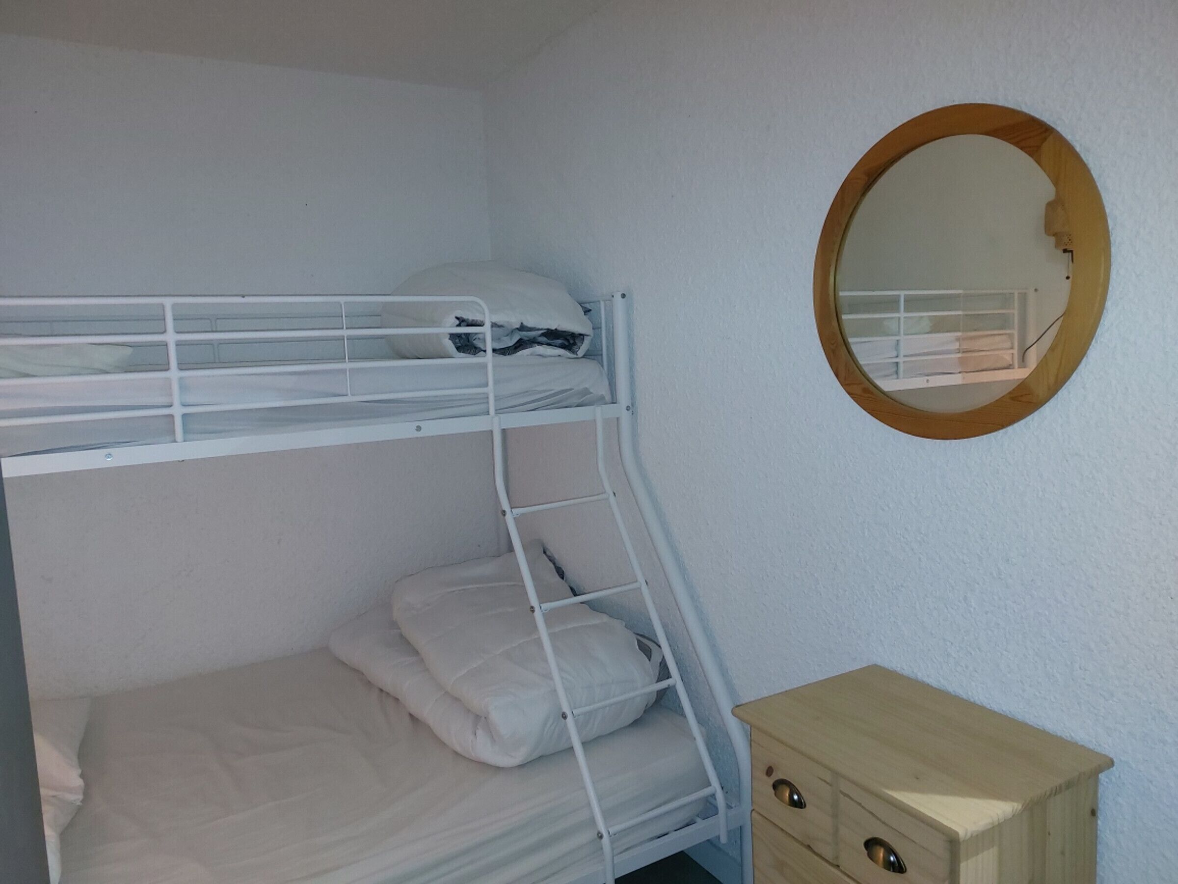 Ein Stockbett mit einem Holzkasten und einem runden Spiegel an der Wand.
