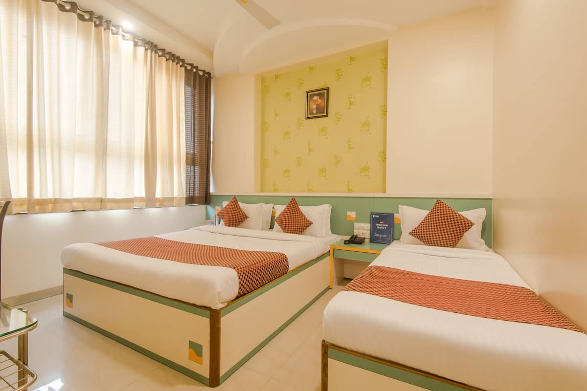 A hotel room with two beds, a small table, and a window with curtains.